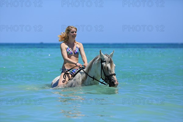 Woman wearing a bikini riding a Barb horse in the sea