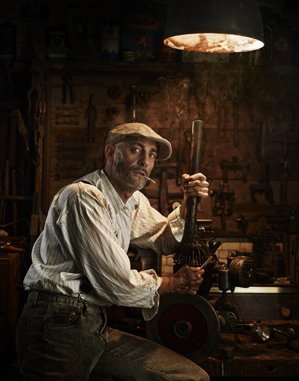 Man with hat and cigarette repairing a motor in a workshop