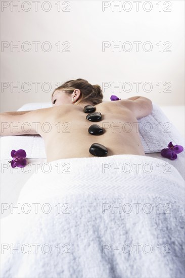 Young woman lying on a massage table and being treated with hot stones