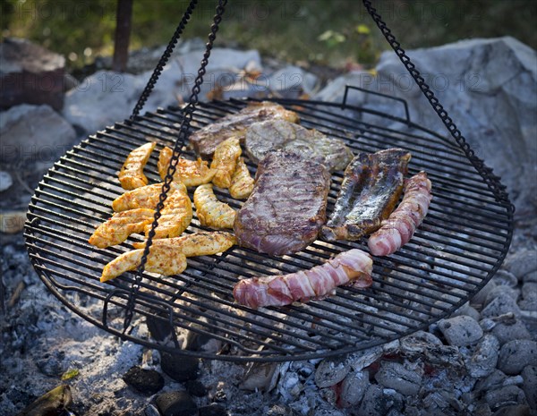 Meat and sausages being cooked on a grill hanging on chains