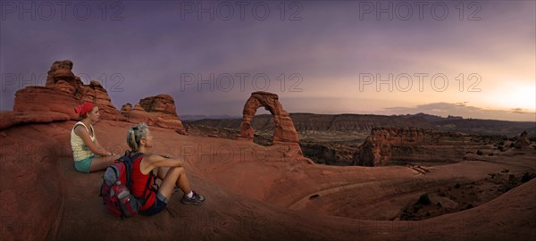 Hikers sitting at Delicate Arch natural stone arch at dusk