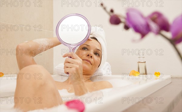 Woman taking a bath and looking at her face with a mirror