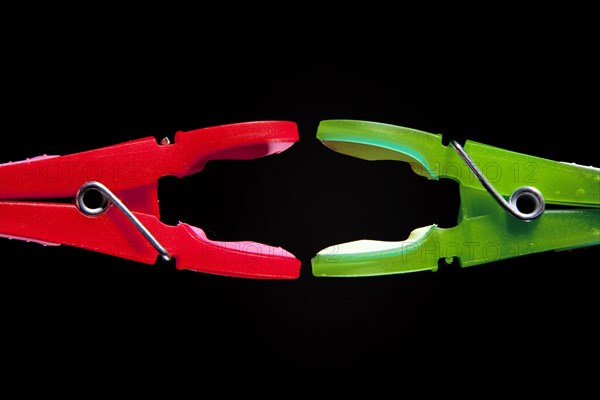 A red clothes-peg and a green clothes-peg are attacking each other