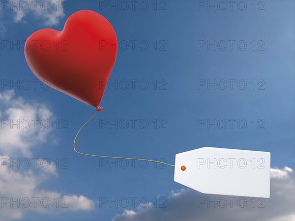 Red balloon in heart shape with tag against blue sky with clouds