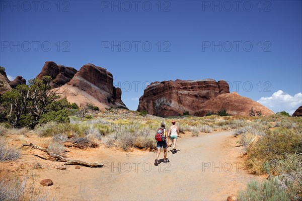 Hikers on a trail in Devil's Garden with sandstone cliffs formed by erosion