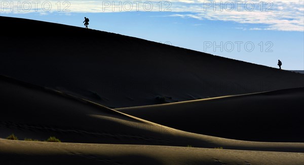 Silhouettes of people climbing a dune