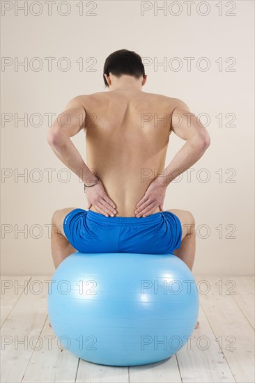 Young man sitting on a gym ball and touching his aching back