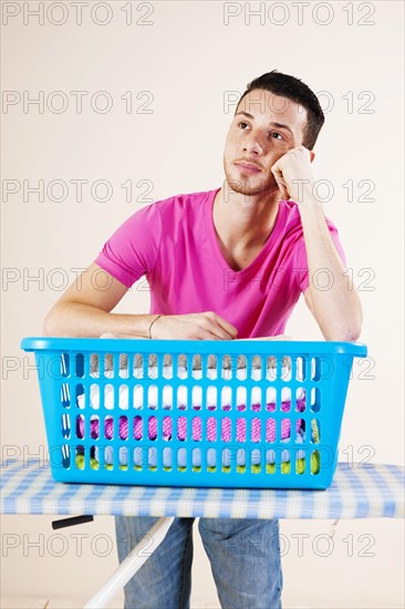 Young man looking desperate while leaning on an ironing board