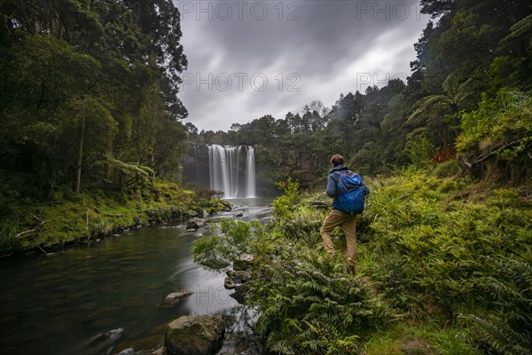 Young man standing in front of waterfall