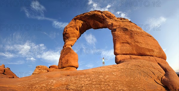 Woman standing under Delicate Arch natural stone arch