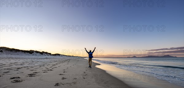 Young man walks on the beach and stretches his arms into the air