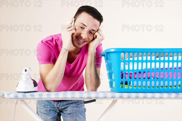 Young man talking on the telephone while leaning on an ironing board