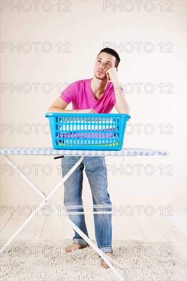 Young man looking desperate while leaning on an ironing board