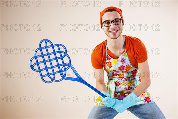Young man wearing an apron and holding a carpet beater