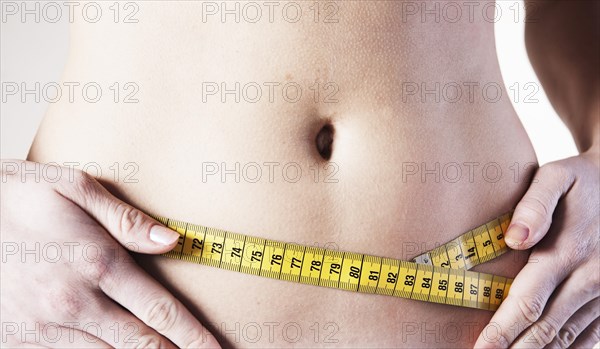 Young woman measuring her waist with a tape measure