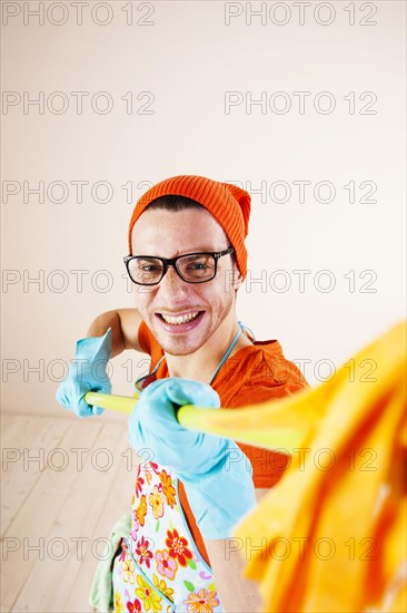 Young man wearing an apron and cleaning gloves holding a cleaning mop