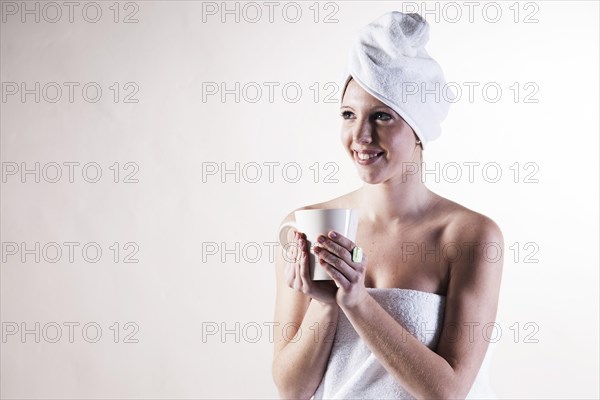 Smiling young woman with a towel wrapped around her head holding a teacup