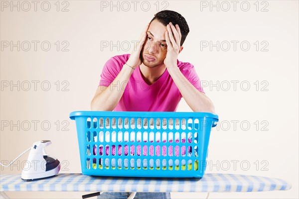 Young man looking desperate while leaning on an ironing board