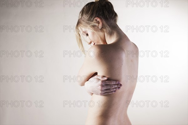 Naked young woman standing with her arms folded