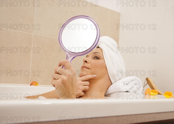 Woman taking a bath and looking at her face with a mirror