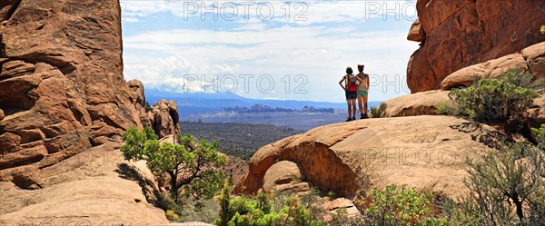 Hikers looking towards the La Sal Mountains from between red sandstone cliffs