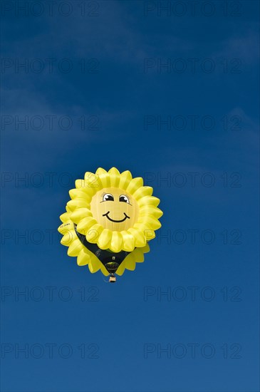 Yellow balloon with a 'smiling sun' or sunflower face against a blue sky