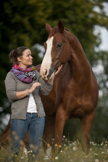 Woman standing next to a Hanoverian horse in a meadow