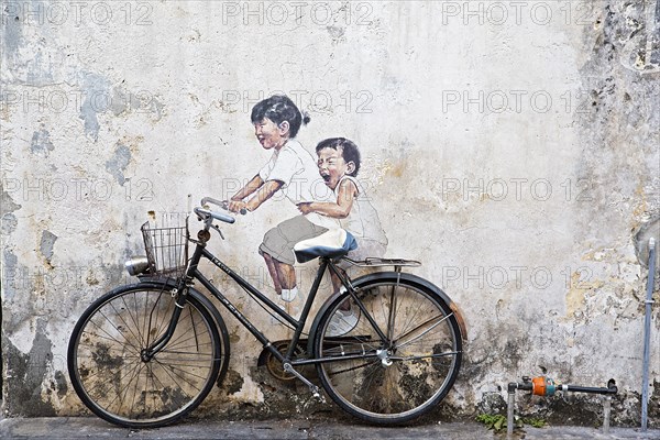 Bicycle in front of house wall with children painted as if they are riding the bike