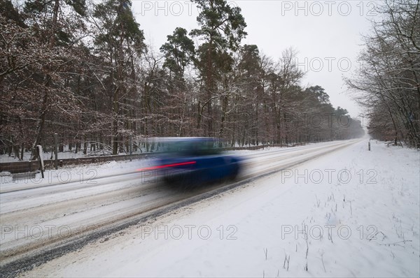 Snow-covered road in winter with car passing by quickly