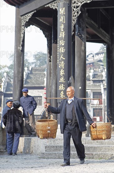 Man shouldering bamboo baskets in front of the Kuixingge Pagoda