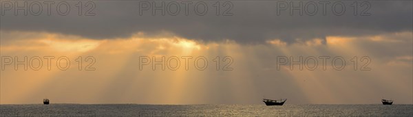 Sun beams above the Arabian Sea with the silhouettes of typical dhows
