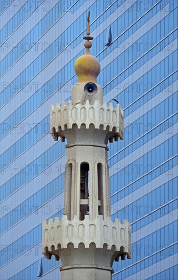 The minaret of a small mosque against the modern glass and steel facade of a skyscraper