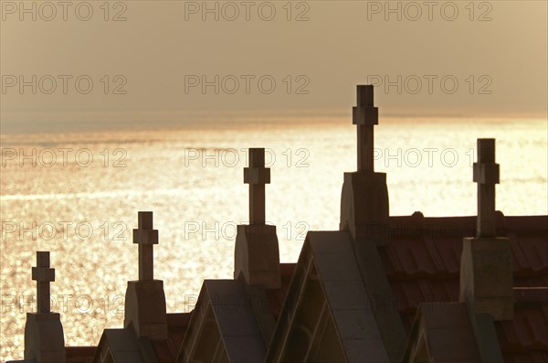 The silhouette of crucifixes of typical above-ground tombs in the cemetery of Ajaccio with the water of the mediterranean sea in the background. Ajaccio is the capital of the mediterranean island of Corsica