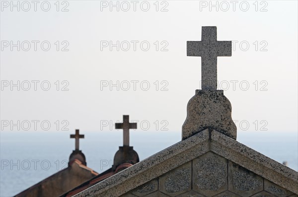 The silhouette of crucifixes of typical above-ground tombs in the cemetery of Ajaccio with the water of the mediterranean sea in the background. Ajaccio is the capital of the mediterranean island of Corsica