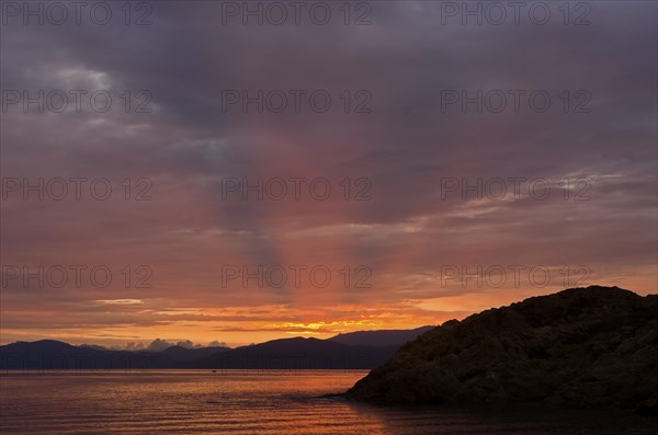 The rising sun forms sun beams behind the rocks of the island Ile de la Pietra near L'Ile-Rousse. L'Ile-Rousse is in the department Haute-Corse