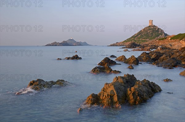 The genoese tower Tour de la Parata at the right and the islands Les Iles Sanguinaires behind the rocky mediterranean coast illuminated by warm morning light. Les Iles Sanguinaires are in the department Corse-du-Sud