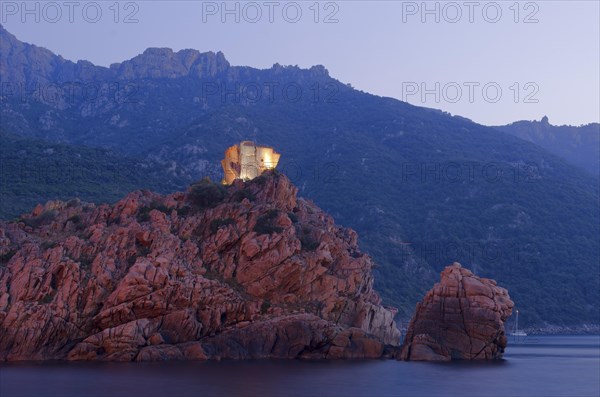 The flood lit Genoese Tower of Porto on top of a rocky hill and the Gulf of Porto at the blue hour