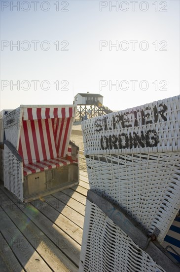 Roofed wicker beach chairs on the beach in front of a house on stilts