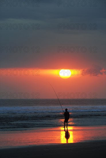 Fisherman fishing at sunset on the beach