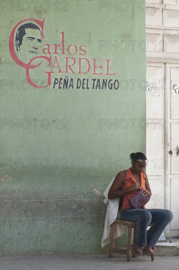 Young woman sitting against a wall with a portrait of Carlos Gardel