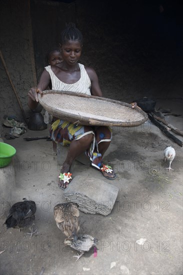 Woman separating grain from the chaff outside a hut