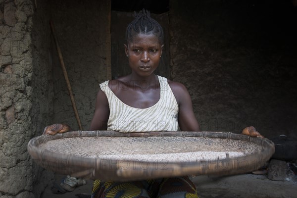 Woman separating grain from the chaff outside a hut