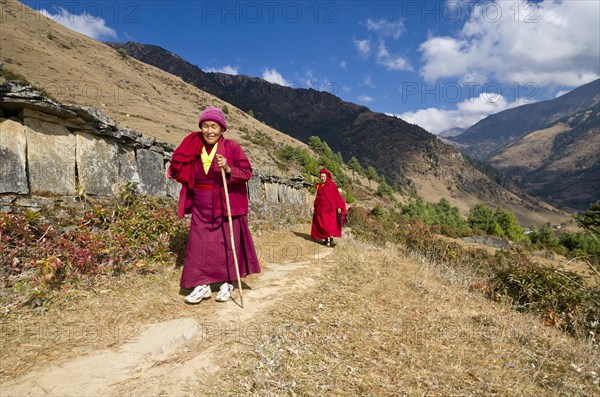 Monks and nuns wearing red cloths walking on a small path along a mountain slope