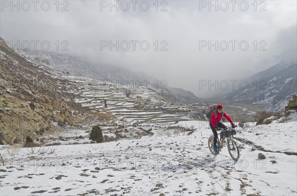 Cyclist riding his bike in the snow up towards Thorong La Pass (5416 m)