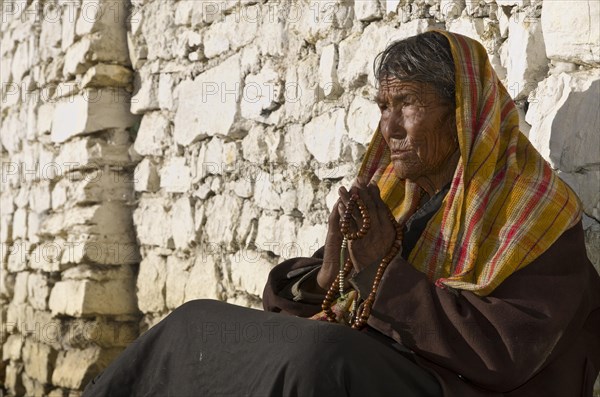 Old local woman praying in front of a brick wall