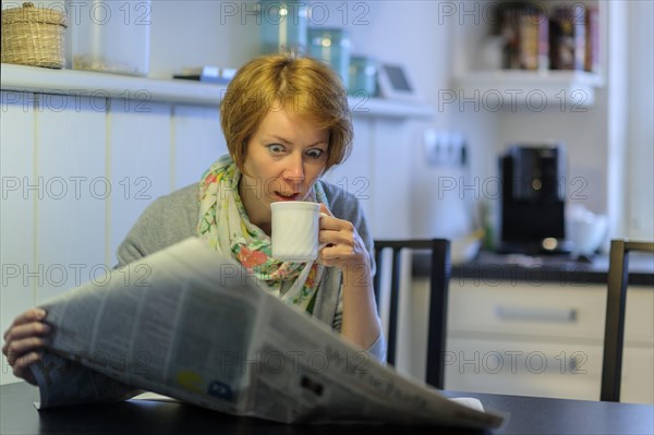 Woman sitting at the kitchen table reading the newspaper