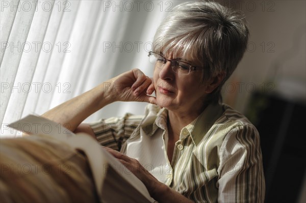 Senior woman sitting at the window and reading a book