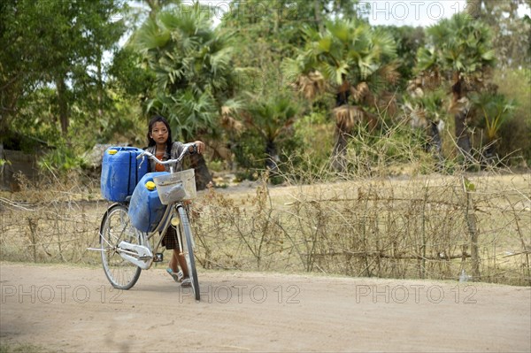 Girl transporting two canisters with water from the reservoir of the nearby pagoda on her bike to her home