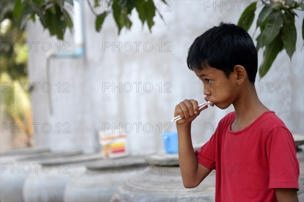 Young boy brushing his teeth outside a house