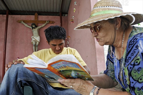 Elderly woman with sun hat teaching a young migrant to read